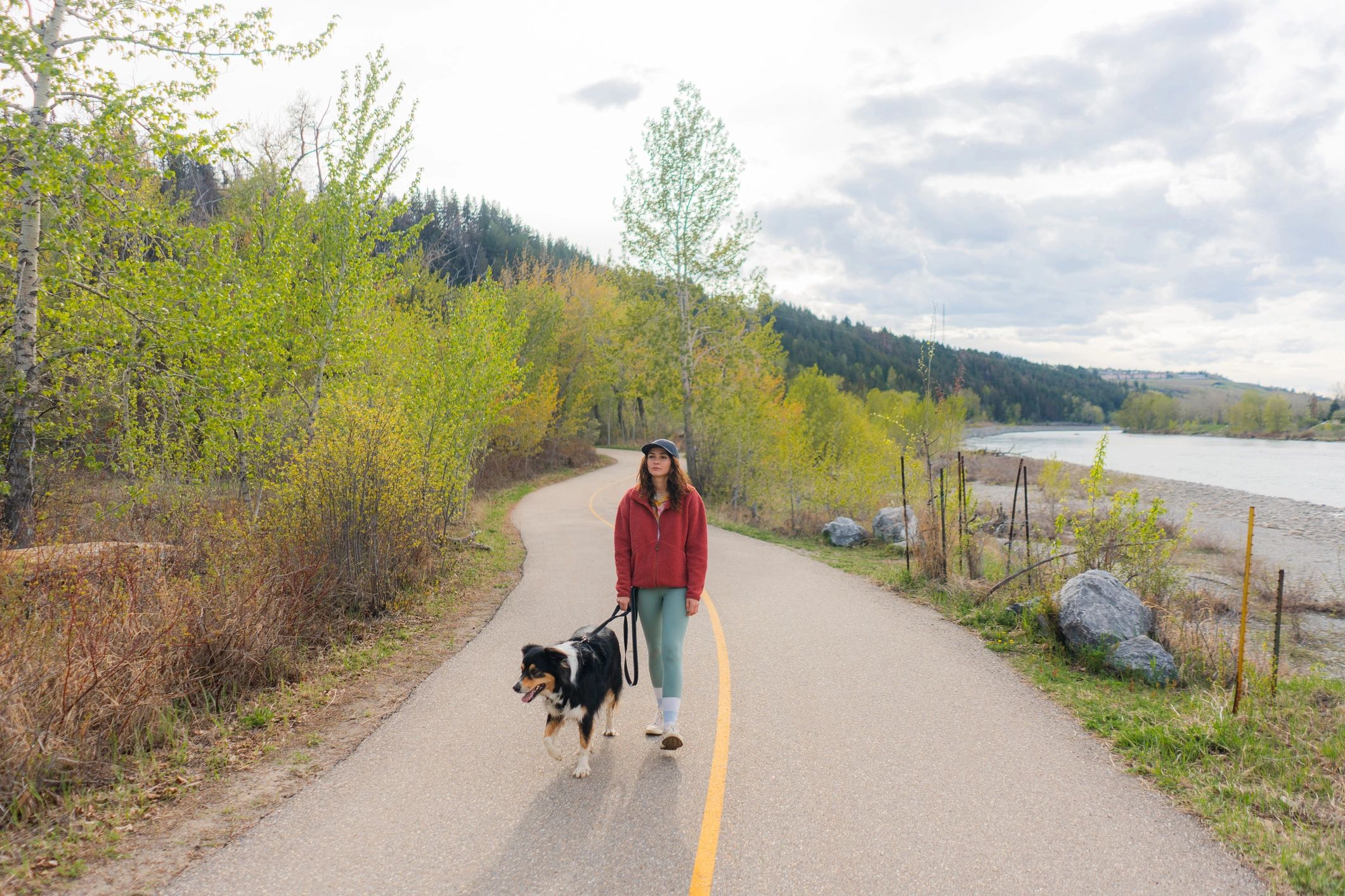 Woman walking an Australian shepherd near a river